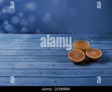 Verre à jus d'orange avec orange divisé en deux sur bois et un arrière-plan lumineux Banque D'Images