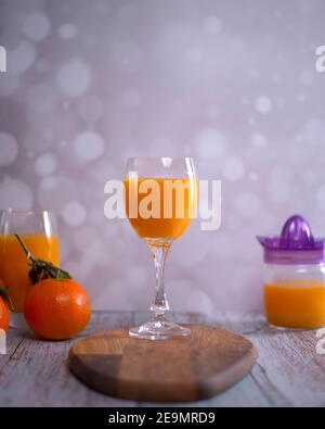 Verre de jus d'orange. Centrifugeuse en verre, jus d'orange, orange de table en bois avec feuilles vertes fond clair Banque D'Images