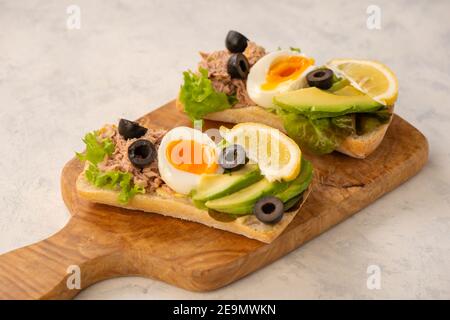 Sandwichs au thon, aux œufs, aux olives et à l'avocat sur fond clair. Banque D'Images