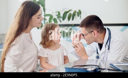 Homme médecin pédiatre examinant une fille malade triste de Kid lors d'une visite médicale avec mère à l'hôpital. Médecin de famille de sexe masculin examinant et consultant pour Banque D'Images