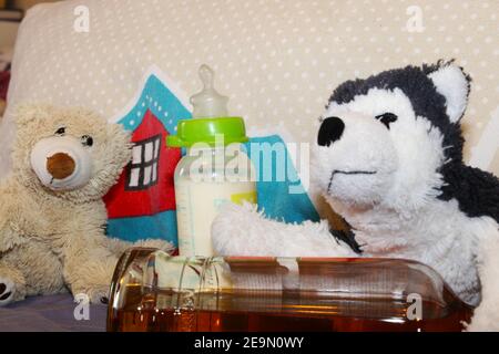 Image symbole de la dépendance à l'alcool chez les parents : jouets en peluche, bouteille pour bébé et alcool Banque D'Images