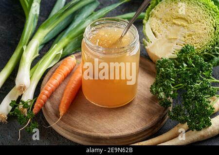 Le bouillon d'os de bœuf congé a été refroidi dans un pot en verre, avec des légumes en arrière-plan Banque D'Images