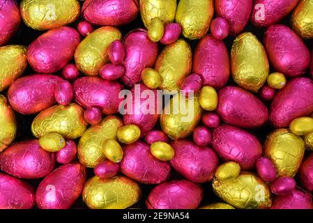 Pile ou groupe de plusieurs couleurs et différentes tailles d'oeufs de pâques au chocolat enveloppés de papier d'aluminium coloré en jaune, or et rose. Banque D'Images