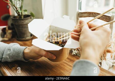 Gros plan des nouilles dans une boîte. Plats à emporter. La personne mange de la nourriture avec des baguettes. Banque D'Images