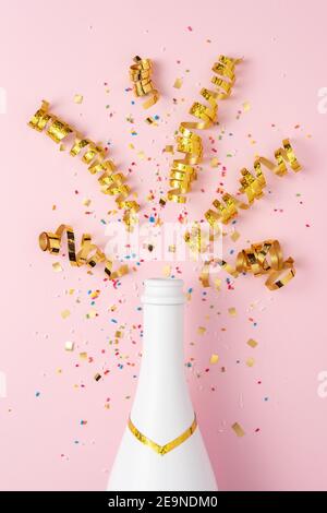 Bouteille de champagne blanche avec confettis et banderoles de fête sur fond rose. Concept de fête minimal. Banque D'Images