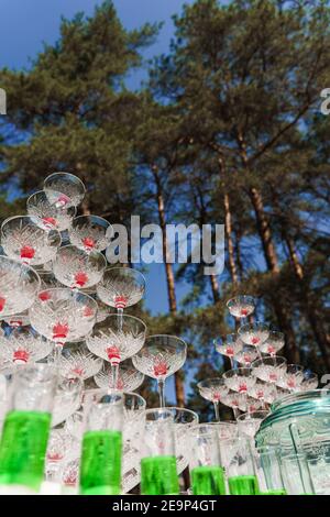 Buvez un cocktail pour votre mariage. Grande pyramide de verres avec champagne et cerise rouge à l'intérieur lors d'une réunion d'affaires le jour d'été dans la forêt. Banque D'Images