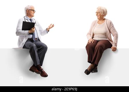 Prise de vue en longueur d'un médecin mature assis sur un panneau vierge et parler à une patiente âgée isolée sur fond blanc Banque D'Images