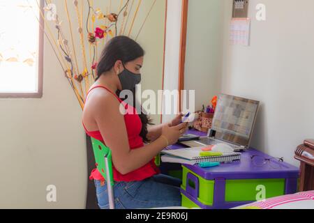 une jeune femme en masque regarde tout son smartphone étudier de chez vous dans une pièce bien lumineuse Banque D'Images