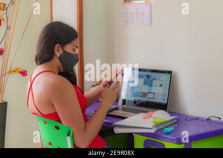 une jeune femme en masque regarde tout son smartphone étudier de chez vous dans une pièce bien lumineuse Banque D'Images