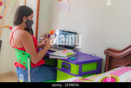 une jeune femme en masque regarde tout son smartphone étudier de chez vous dans une pièce bien lumineuse Banque D'Images