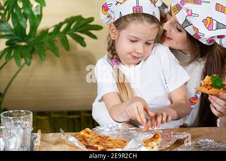 Une conversation de mère et de fille de cinq ans pleine d'amour et d'affection tout en mangeant de la pizza maison. La joie des moments passés ensemble par la mère et la fille tout en mangeant. Banque D'Images