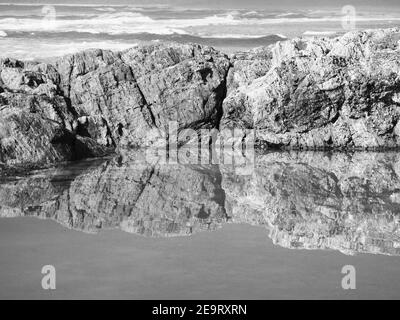 De magnifiques reflets. Les rochers bordant la piscine se réfléchit et se reflétaient dans l'eau salée, en regardant au-delà de l'océan Pacifique. Monochrome Banque D'Images