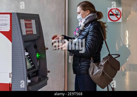 Une femme portant un masque médical de protection sur son visage insertion d'une carte bancaire et retrait d'espèces d'un ATM Banque D'Images