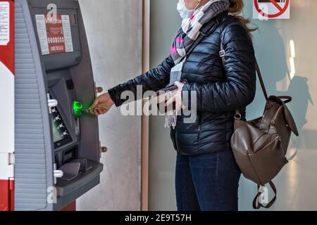 Une femme portant un masque médical de protection sur son visage insertion d'une carte bancaire et retrait d'espèces d'un ATM Banque D'Images
