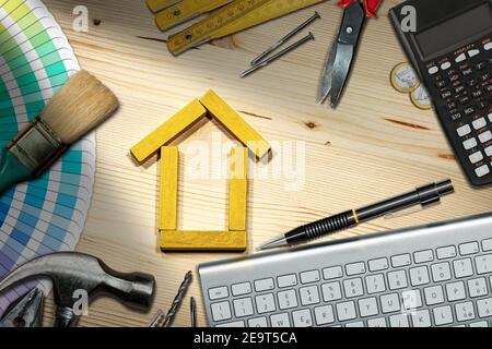 Petite maison en bois faite de blocs de jouets sur le bureau, avec des outils de travail, un clavier d'ordinateur, une calculatrice et des pièces en euros. Concept d'amélioration de la maison. Banque D'Images