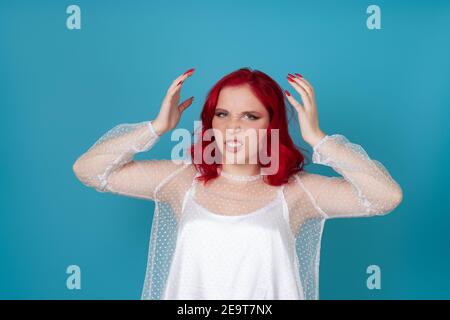 une femme frustrée, en colère dans la robe de soie blanche et avec les cheveux rouges, elle se livre à la tête avec les mains du ressentiment et de l'insulte Banque D'Images