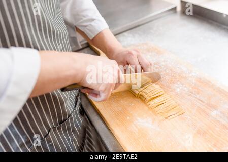 Couper les nouilles dans la cuisine . Le chef cuisent des spaghetti au restaurant. Le chef coupe avec un couteau des nouilles crues avec de la farine Banque D'Images