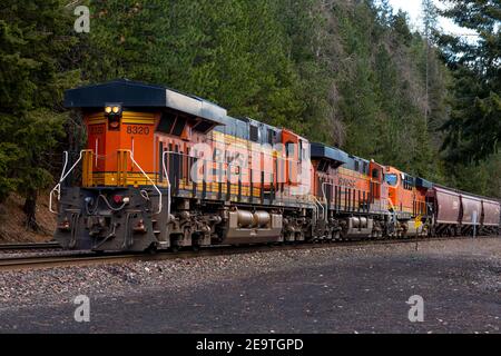 Trois locomotives tracées d'un train de marchandises à trémie couverte BNSF descendant les voies dans la ville de Troy, Montana. Burlington Nord et Banque D'Images