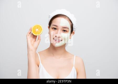 Belle femme obtient masque d'argile facial et tenant des morceaux d'orange sur fond blanc. Concept beauté, soins du corps et spa Banque D'Images