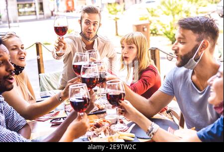 Des amis toastent du vin rouge au bar du restaurant avec des masques pour le visage - Nouveau concept d'amitié normale avec des gens heureux ayant du plaisir ensemble par beau temps Banque D'Images