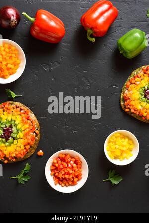 Cadre de pizza aux poivrons de légumes et ingrédients sur fond de pierre noire. Végétalien végétarien ou concept de nourriture saine. Plat alimentaire sans gluten. Banque D'Images