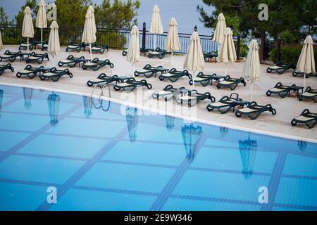 Des chaises longues en plastique et des parasols sont mis à votre disposition pour la protection du soleil sur les carreaux près de la piscine dans l'espace de loisirs Banque D'Images