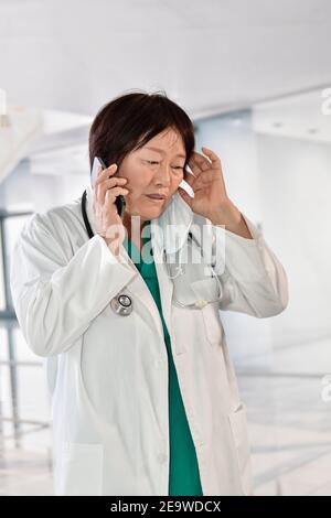 Femme asiatique médecin écoutant son téléphone tout en mettant sa main sur son front en désespoir de cause. Mise au point sélective. Concept de stress et de soins de santé. Banque D'Images