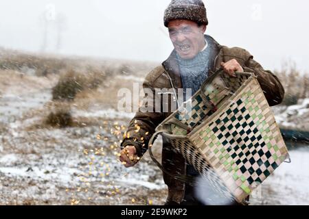 (210206) -- GUIYANG, 6 février 2021 (Xinhua) -- photo prise le 1er janvier 2013 montre Zang Erjun (décédé en mars 2017) dispersant de la nourriture pour les oiseaux contre un blizzard à la réserve naturelle nationale Caohai dans le comté autonome de Yi, hui et Miao de Weining, dans la province de Guizhou, au sud-ouest de la Chine. Créée en 1992 en tant que réserve naturelle nationale, la réserve naturelle nationale Caohai couvre une superficie de plus de 120 000 kilomètres carrés. Au cours des dernières années, plus de 60 000 personnes ont servi de Rangers de la réserve, nourrissant des oiseaux, observant les activités des oiseaux et patrouilant dans la réserve. Jour après jour, le à Banque D'Images