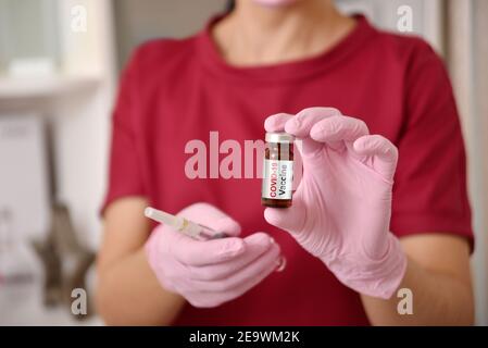 Femme médecin en vêtements rouges et gants roses tenant une seringue et un vaccin contre le coronavirus. Santé et concept médical. Banque D'Images