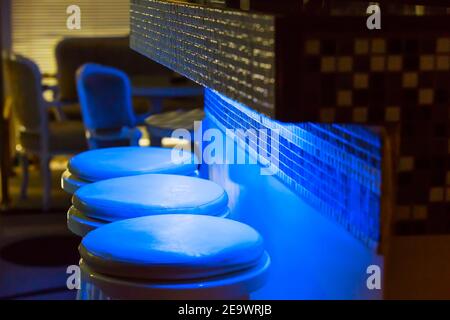 Vider les chaises de bar le long du comptoir éclairé par une lumière bleue Banque D'Images