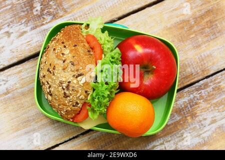 Boîte à lunch saine contenant un rouleau de fromage brun avec de la laitue et de la tomate, de la pomme et du satsuma Banque D'Images