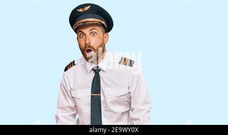 Beau homme avec la barbe portant l'uniforme pilote d'avion peur et choqué avec l'expression surprise, la peur et le visage excité. Banque D'Images