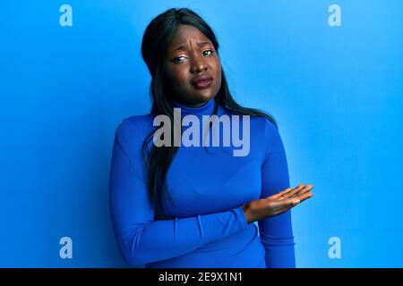 Jeune femme africaine se présentant avec la paume ouverte sur le côté dans le visage de choc, regardant sceptique et sarcastique, surpris par la bouche ouverte Banque D'Images