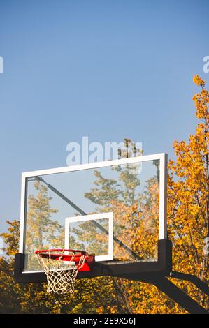 Panier de basket-ball avec filet et planche transparente dans le parc d'automne avec ciel bleu Banque D'Images