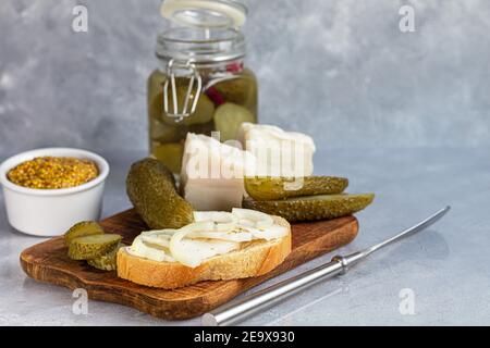 Des concombres marinés dans un pot en verre sur une planche de bois et un sandwich au bacon. Haricots moutarde en arrière-plan. Aliments fermentés. Copier l'espace. Banque D'Images