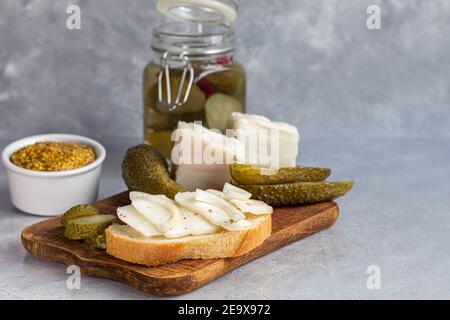 Des concombres marinés dans un pot en verre sur une planche de bois et un sandwich au bacon. Haricots moutarde en arrière-plan. Aliments fermentés. Copier l'espace. Banque D'Images