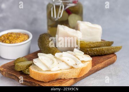 Des concombres marinés dans un pot en verre sur une planche de bois et un sandwich au bacon. Haricots moutarde en arrière-plan. Aliments fermentés. Copier l'espace. Banque D'Images