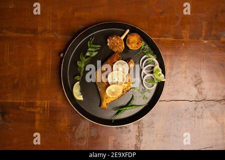 poisson frite de pomfret - profondément frits deux poissons de pomfret qui est bien garni de citron et d'oignon dans une céramique blanche plaque avec fond en bois Banque D'Images