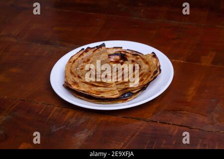 Aloo Paratha / pain plat farci de pommes de terre indiennes dans une assiette blanche. Sur une table en bois. Banque D'Images