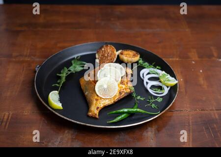 poisson frite de pomfret - profondément frits deux poissons de pomfret qui est bien garni de citron et d'oignon dans une céramique blanche plaque avec fond en bois Banque D'Images