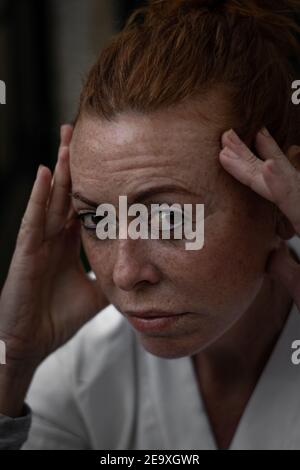 Une femme aux cheveux rouges estime l'âge de 50 ans en T-shirt blanc inquiet et concentrée Banque D'Images