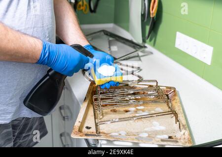 un homme applique un agent de nettoyage à une éponge à nettoyez les plaques de cuisson sales et les grilles de la graisse Banque D'Images