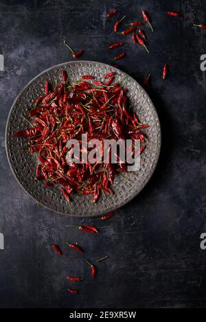 Vue de dessus de pile de piments rouges chauds séchés placé sur l'assiette et éparpillé sur une table en marbre gris Banque D'Images