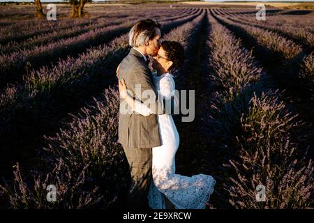 Vue latérale en grand angle sur le visage romantique d'un couple récemment mariés pour faire face à des baisers sur un terrain spacieux contre un ciel de coucher de soleil violet Banque D'Images