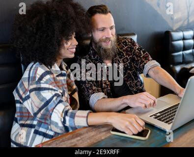 Contenu couple multiethnique de freelances assis à table avec ordinateur portable et travailler ensemble sur le projet dans le café Banque D'Images