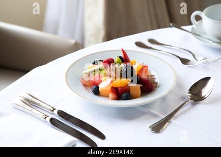 Au-dessus de la savoureuse salade de fruits avec assortiment de baies kiwi et pastèque servie sur une assiette blanche sur la table avec une tasse de café et de couverts à l'hôtel resta Banque D'Images