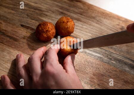 Du dessus de la récolte anonyme cuisinier couper croustillants frits profonds boule de fromage sur planche à découper en bois Banque D'Images