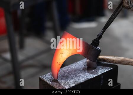 Forgeron sans visage de récolte tenant le métal chaud détail de la hache viking avec des pinces tout en travaillant dans forge Banque D'Images