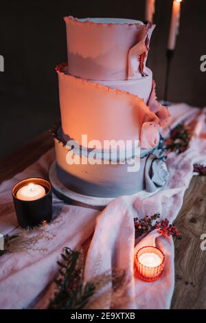Délicieux gâteau étagé servi sur une table en bois et entouré par bougies allumées dans la pièce sombre Banque D'Images