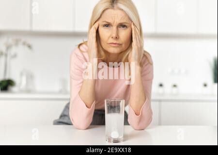 Le comprimé de soulagement de douleur effervescente se dissout dans le verre d'eau, une femme d'âge moyen dans hors foyer souffrant de maux de tête, tenant la tête, massages le Banque D'Images